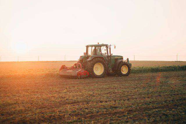 Green tractor with mower attachment silhouetted at sunset