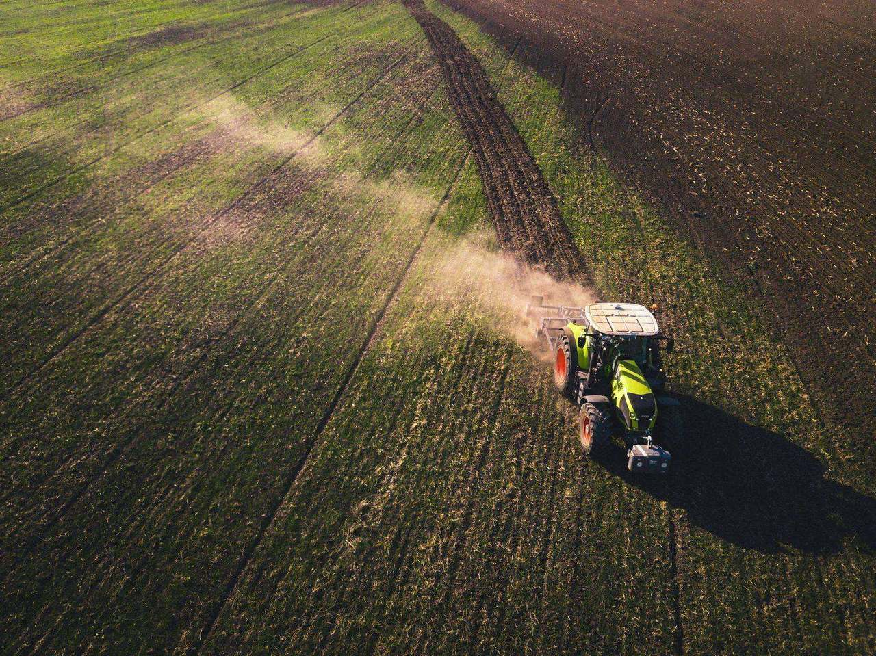 Aerial view of green tractor tilling soil, dust trailing
