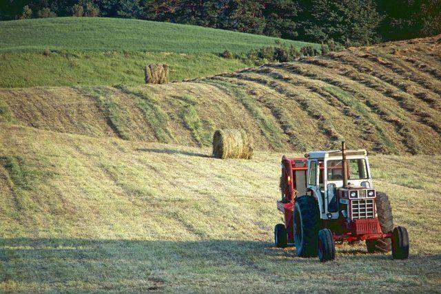 Red tractor beside hay bales in rolling hillside field