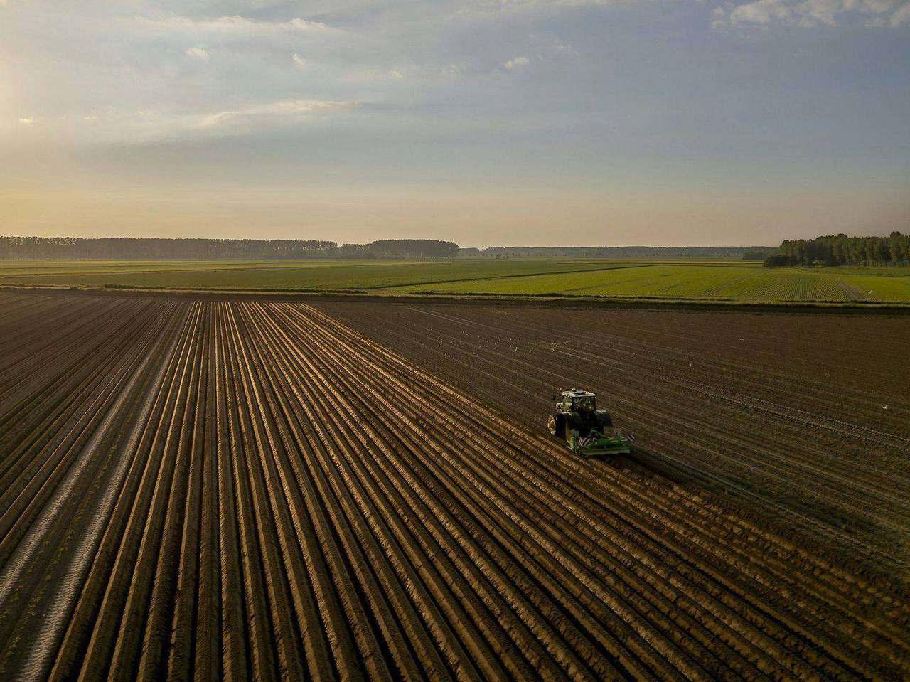 Aerial tractor working furrowed field in hazy light